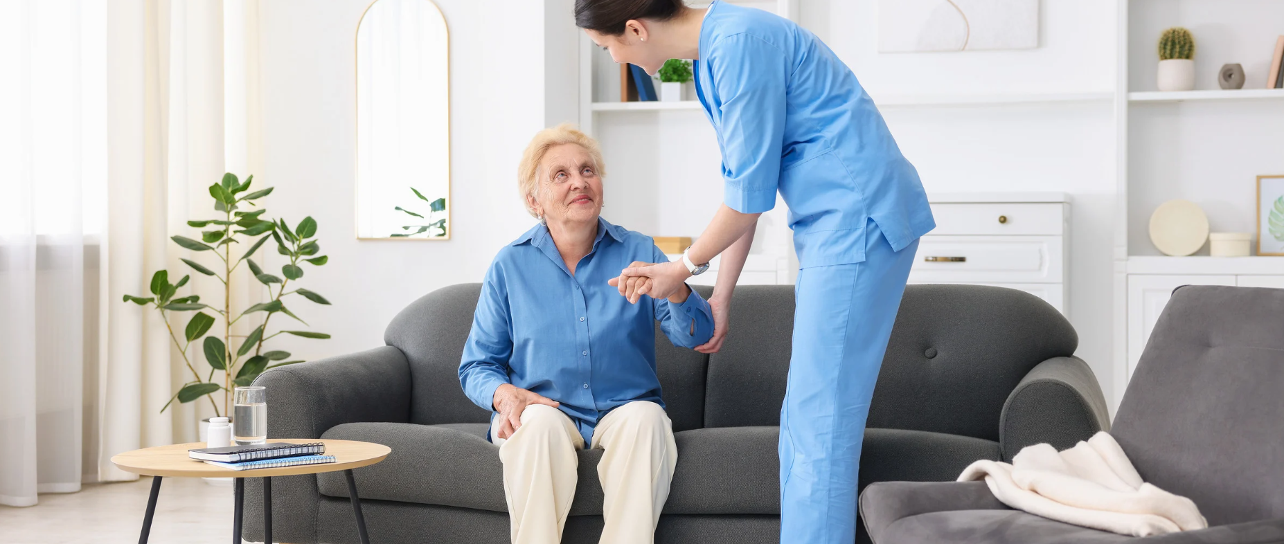 Senior receiving assistance from caregiver while standing up from couch at home